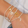 Multiple bracelets with charms on a wrist against a neutral background