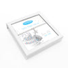 A square white gift box with a hinged lid, shown open on a white background. Inside is a silver chain bracelet with a star charm and a printed card featuring a teddy bear illustration and blue text.