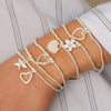 Multiple bracelets with heart, star, and flower charms on a wrist against a striped background