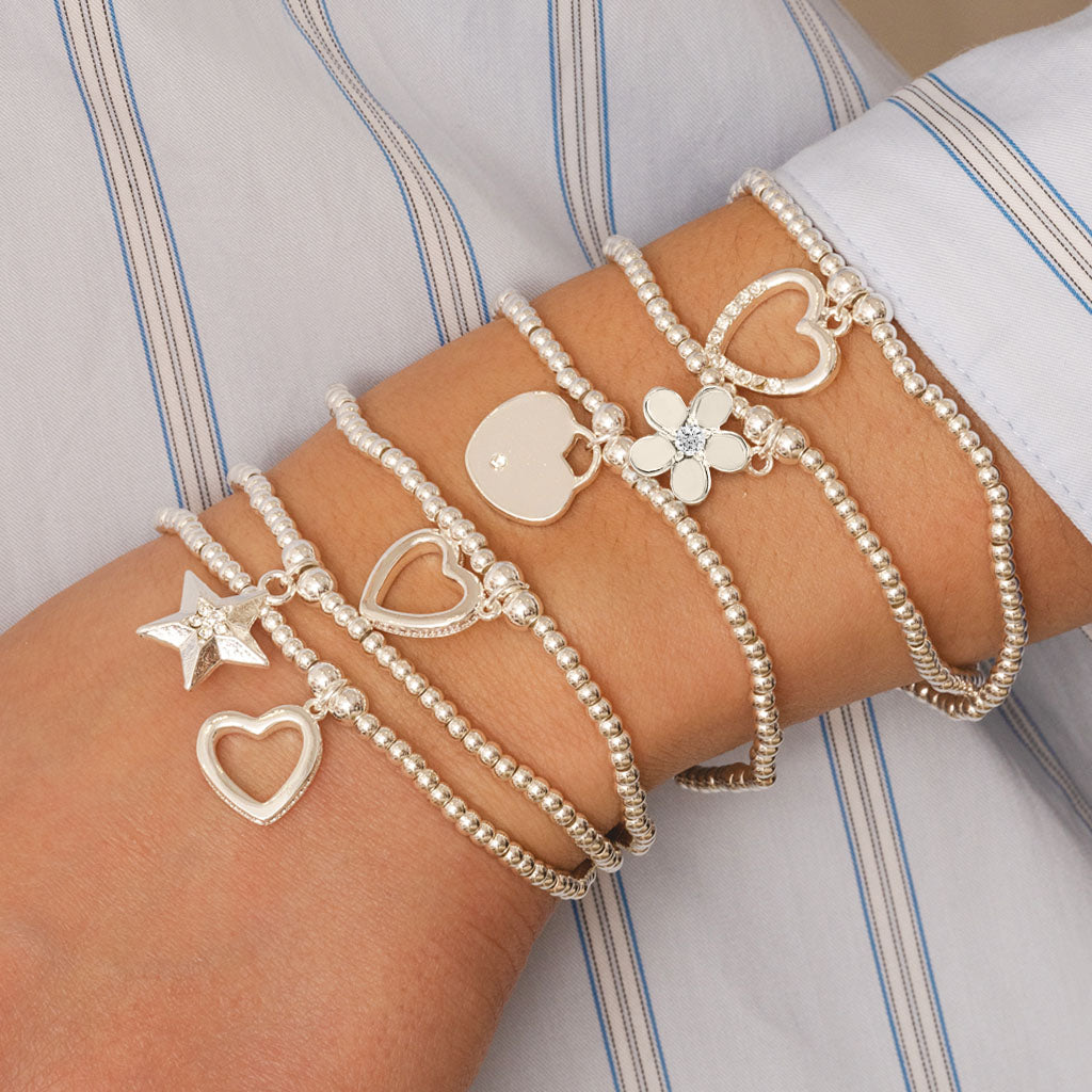 Multiple bracelets with heart, star, and flower charms on a wrist against a striped background
