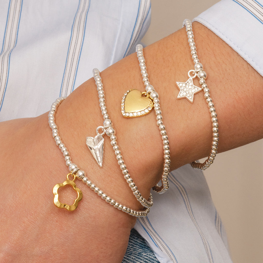 Close-up of a wrist wearing multiple beaded bracelets with various charms on a neutral background.