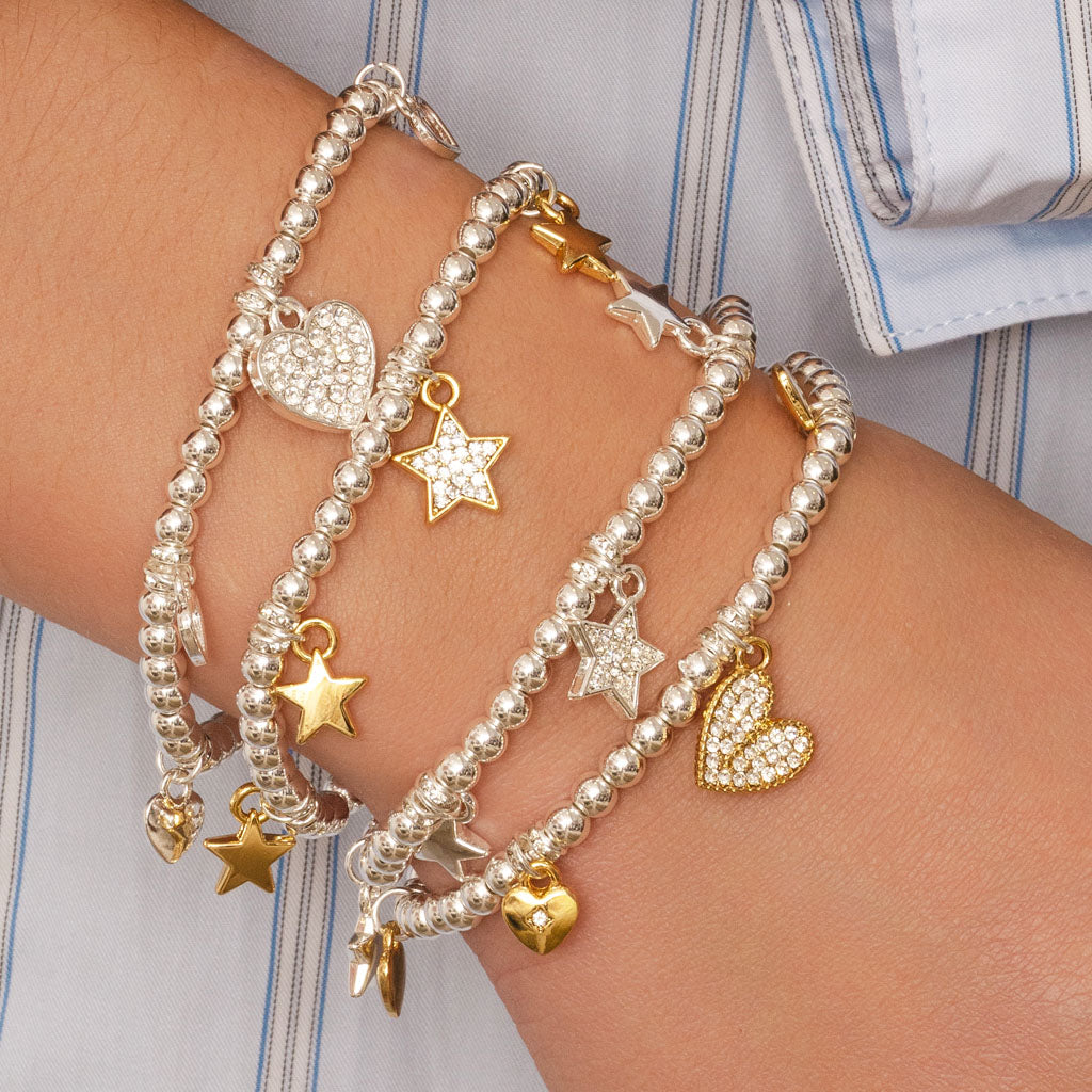Multiple beaded bracelets with heart and star charms on a wrist against a striped shirt background.