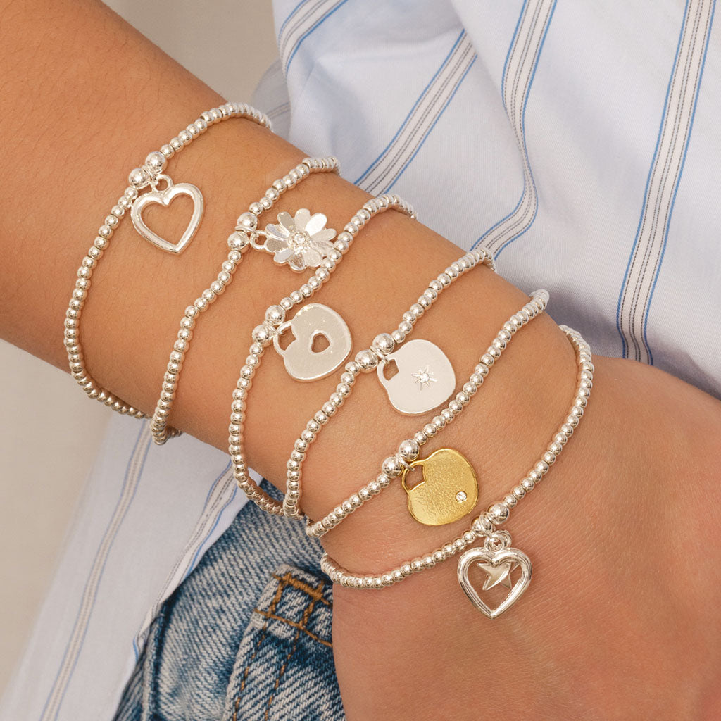 Multiple pearl bracelets with various charms on a wrist, wearing a denim jacket.